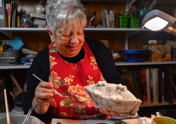 Photo shows Adrina looking at a piece in progress after finishing glazing details on the bottom.