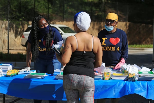 Jocelyn Watkins (left) and Monica Boykin (right) give school supplies and talk to a community member at the Grab and Go free food and groceries event on Friday, April 17, 2020, at Allen Hills Apartments in Atlanta. The community effort to help families during the COVID-19 pandemic was led by the Fulton County district attorney’s office. (Christina Matacotta, for The Atlanta Journal-Constitution)