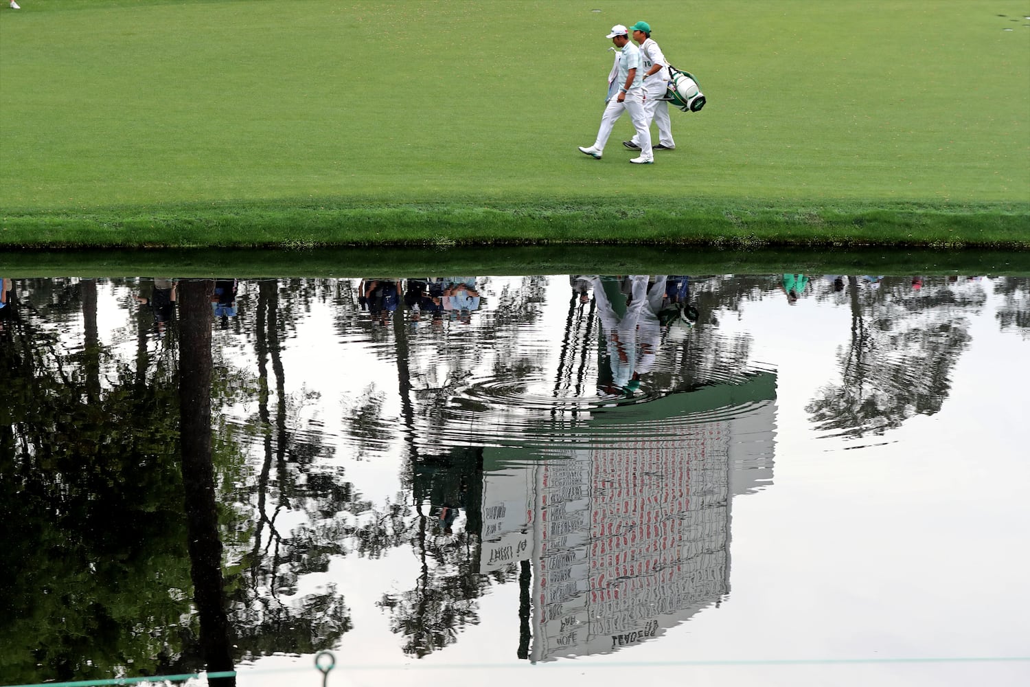 April 10, 2021, Augusta: Hideki Matsuyama and his caddie Shota Hayafuki walk to the sixteenth green with the scoreboard reflected in the pond during the third round of the Masters at Augusta National Golf Club on Saturday, April 10, 2021, in Augusta. Curtis Compton/ccompton@ajc.com