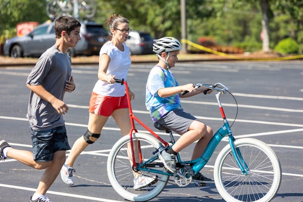 Volunteers Jack Reagin and Niam Goggin helped special-needs camper Rylan learn how to ride a two-wheel bike without adaptations during the iCan Bike Alpharetta camp at The Cooler in Alpharetta.  PHIL SKINNER FOR THE ATLANTA JOURNAL-CONSTITUTION.