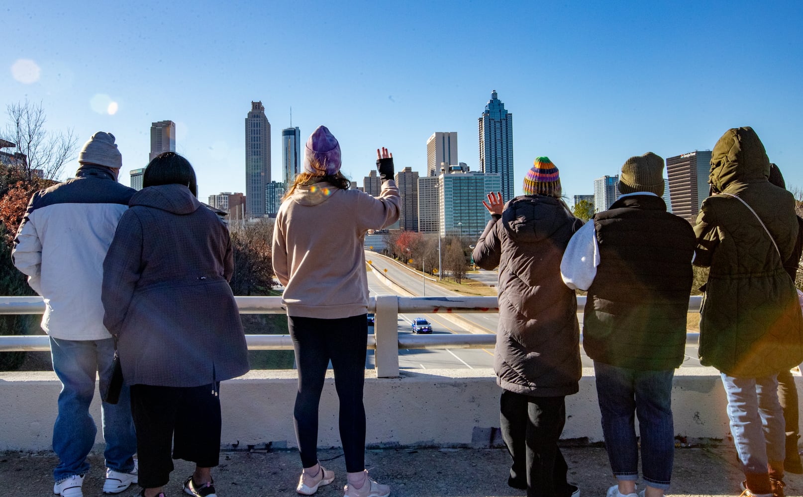 The body of Jimmy Carter is carried from the Georgia Capitol to the Carter Center on Freedom Parkway under the Jackson Street Bridge on Saturday, Jan 4, 2025.  Heather Montgomery Rogers, center, pink sweat shirt, of East Atlanta waves as the motorcade passes.  (Jenni Girtman for The Atlanta Journal-Constitution)