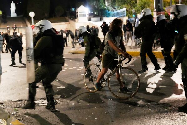 A cyclist passes riot police during clashes, as the Greek opposition parties have challenged the country's center-right government with a censure motion in parliament over a devastating rail disaster nearly two years ago, in Athens, Wednesday, March 5, 2025. (AP Photo/Petros Giannakouris)