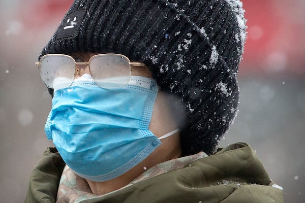 A woman's eyeglasses are fogged up as she wears a face mask during a snowfall in Beijing on Sunday. China’s death toll recently has topped 300 from coronavirus.