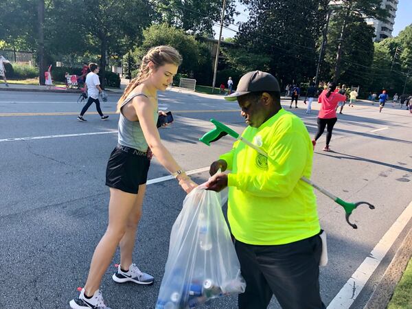 William Robinson collects a plastic water bottle from a participant at the AJC Peachtree Road Race July 4, 2021. Robinson has worked at the race more than 20 times. (AJC photo by Ken Sugiura)