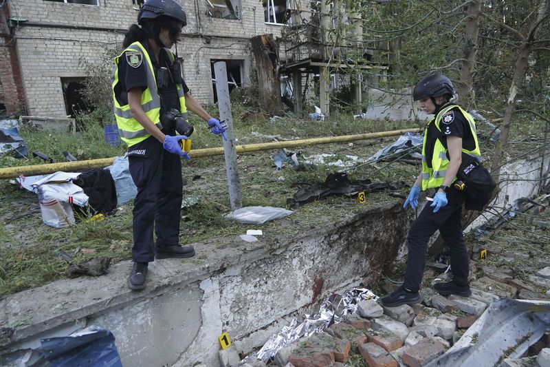Police officers document evidence near to a body of a man who was killed by a Russian attack on Nova Poshta delivery in Kharkiv, Ukraine, Sunday, June 30, 2024. At least one person was killed and several injured. (AP Photo/Andrii Marienko)