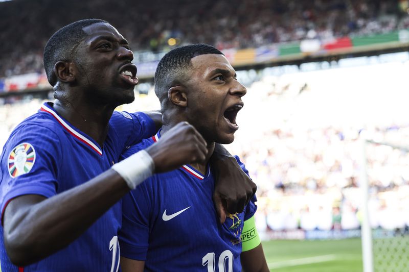 Kylian Mbappe of France, right, celebrates after scoring a penalty kick during a Group D match between the France and Poland at the Euro 2024 soccer tournament in Dortmund, Germany, Tuesday, June 25, 2024. At left is Ousmane Dembele of France. (Friso Gentsch/dpa via AP)