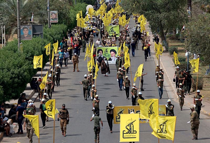 FILE - Iraqi Popular Mobilization Forces march as they hold their flag and posters of Iraqi and Iranian Shiites spiritual leaders during "al-Quds" or Jerusalem Day, in Baghdad, Iraq, June 8, 2018. Thousands of fighters from Iran-backed groups in the Middle East are offering to come to Lebanon to join the militant Hezbollah group in its fight with Israel. (AP Photo/Hadi Mizban, File)