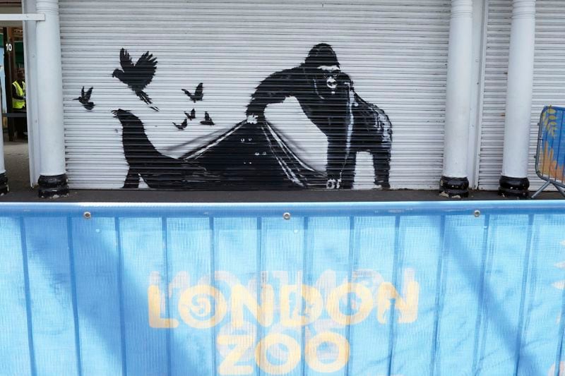 The new artwork unveiled by Banksy at London Zoo, depicting a gorilla lifting up a shutter at the entrance allowing a number of birds to escape, while the eyes of other animals can be seen lurking in the darkness, the ninth artwork in his animal-themed collection, in London, Tuesday Aug. 13, 2024. (Stefan Rousseau/PA via AP)