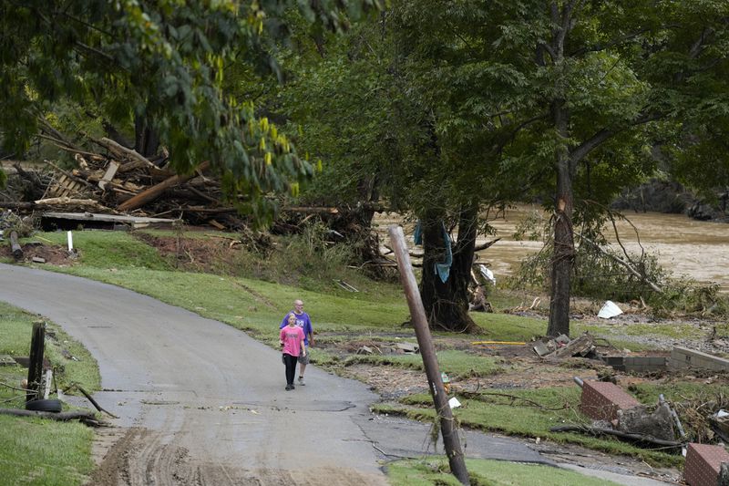 People walk along River St. near the Pigeon River where flood damage is seen Saturday, Sept. 28, 2024, in Newport, Tenn. (AP Photo/George Walker IV)