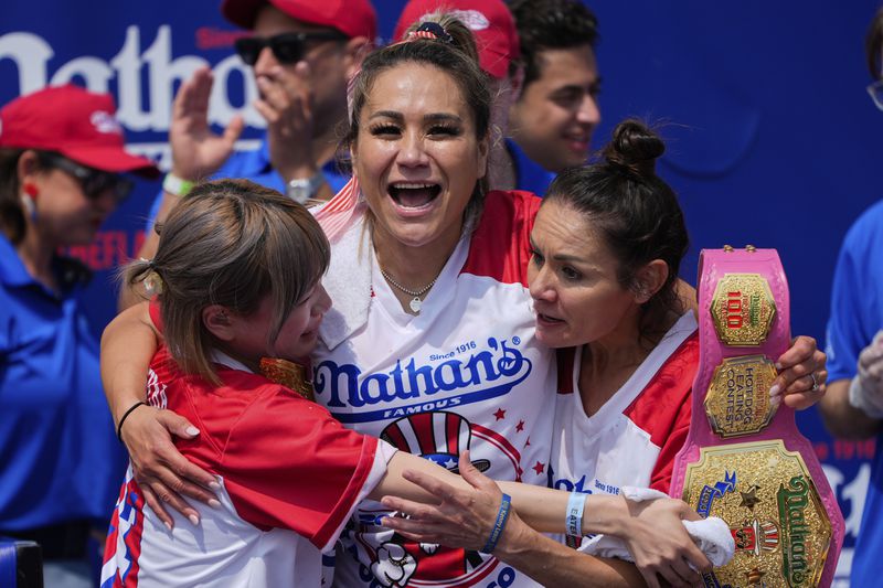 Miki Sudo, center, hugs Mayoi Ebihara, left, and Michelle Lesco, right, after winning the women's division of the Nathan's Famous Fourth of July hot dog eating contest, Thursday, July 4, 2024, at Coney Island in the Brooklyn borough of New York. Sudo ate a record 51 hot dogs. (AP Photo/Julia Nikhinson)