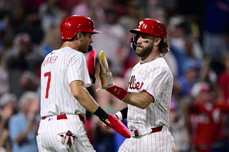 Philadelphia Phillies' Bryce Harper, right, high-fives Trea Turner, left, after they scored on a double hit by Nick Castellanos off Atlanta Braves' Spencer Schwellenbach during the sixth inning of a baseball game, Sunday, Sept. 1, 2024, in Philadelphia. (AP Photo/Derik Hamilton)