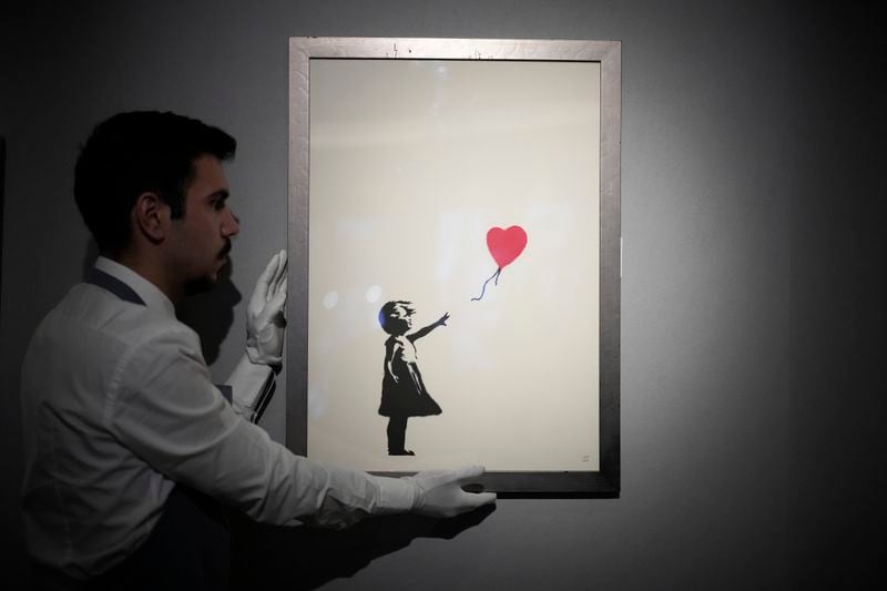 FILE - A staff member poses for photographs with a print of "Girl with Balloon, 2004" by British street artist Banksy, at Bonhams auction house in London, Monday, Nov. 8, 2021. (AP Photo/Matt Dunham, File)