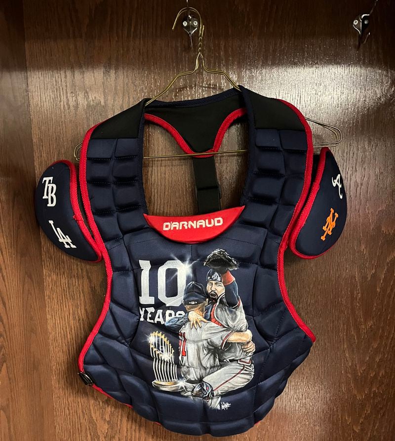 A chest protector hangs in Braves catcher Travis d’Arnaud’s locker in the visiting clubhouse at Wrigley Field. The protector was among the gifts Braves teammates gave d'Arnaud on the occasion of his 10th anniversary of major league service time, which he reached Aug. 4, 2023. (Photo by Justin Toscano/The Atlanta Journal-Constitution)