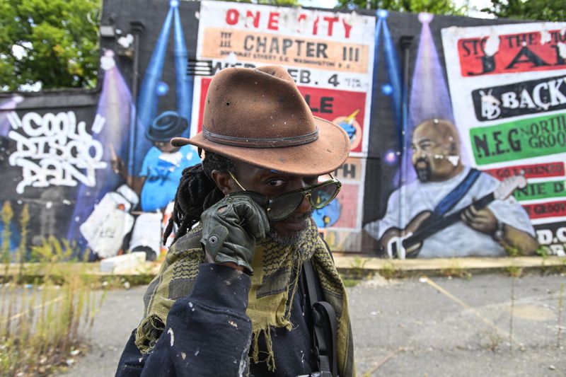 Mural artist Eric B. Ricks poses for a portrait in front of a mural that he oversaw and instructed young artist to paint in 2017 , Monday, Sept. 16, 2024, in Washington. (AP Photo/John McDonnell)