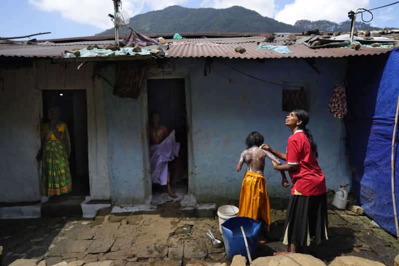 Muthuthewarkittan Manohari, a tea plantation worker, right, bathes her younger daughter Madubhashini, as her elder daughter Shalani, center, stands at the doorway of their small house in Spring Valley Estate in Badulla, Sri Lanka, Monday, Sept. 9, 2024. (AP Photo/Eranga Jayawardena)