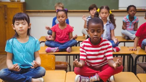Pupils meditating in lotus position on desk in classroom. (Shutterstock)
