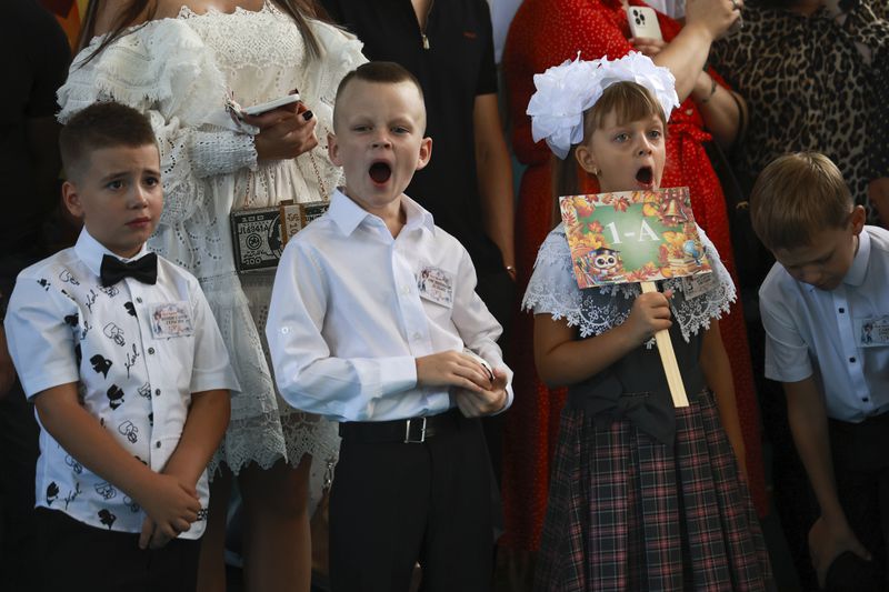 First graders yawn as they attend a ceremony marking the start of classes at a school as part of the traditional opening of the school year known as "Day of Knowledge" in Makiivka, Russian-controlled Donetsk region, eastern Ukraine, on Monday, Sept. 2, 2024. (AP Photo/Alexei Alexandrov)