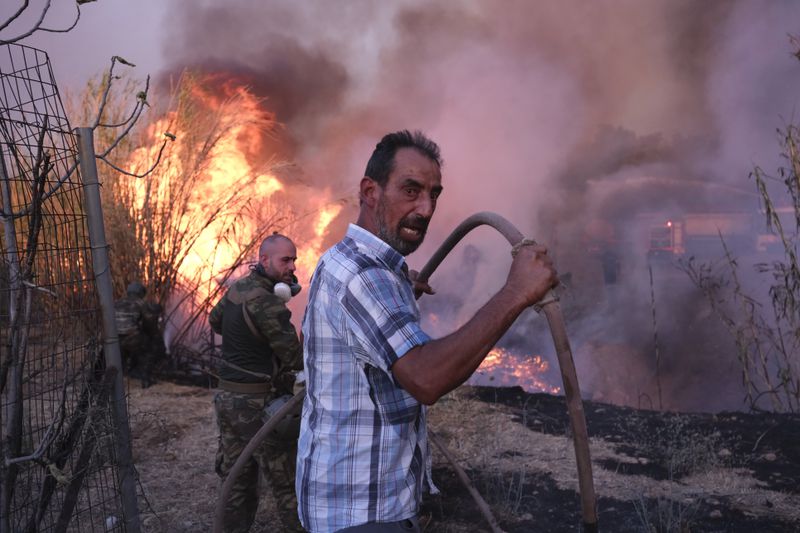 Volunteers try to extinguish the fire in northern Athens, Monday, Aug. 12, 2024, as hundreds of firefighters tackle a major wildfire raging out of control on fringes of Greek capital. (AP Photo/Aggelos Barai)