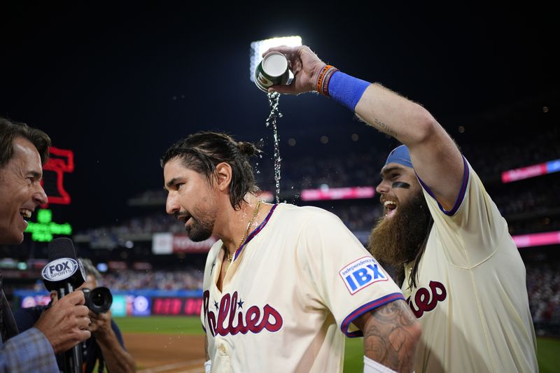 Philadelphia Phillies' Brandon Marsh, right, pours water over Nick Castellanos, center while he is interviewed after the Phillies won Game 2 of a baseball NL Division Series against the New York Mets, Sunday, Oct. 6, 2024, in Philadelphia. (AP Photo/Matt Slocum)