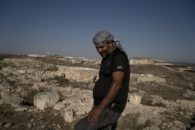 Hassan Battat stands in the West Bank village of Khirbet Zanuta, near his home, rear left, overlooking the Meitarim settlement, Thursday, Aug. 29, 2024. Ten months after settlers threatened to kill them if they didn't leave this village, some Palestinian residents are finally home, under a rare court order. (AP Photo/Maya Alleruzzo)