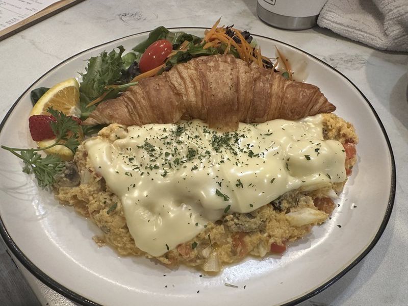 An order of tom yum scramble -- eggs mixed with Dungeness crab, Thai style tom yum sauce, Swiss cheese, onion, mushrooms, tomato with a croissant -- sits on a counter at Taste & Glory restaurant in San Mateo, Calif, on Saturday, Aug. 17, 2024. (AP Photo/Terry Tang)