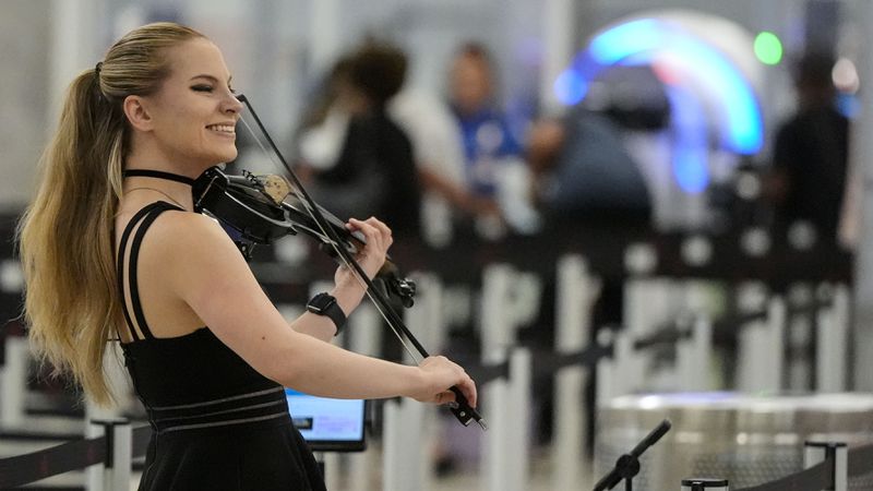 Michelle Winters plays the violin as passengers stand in line at Hartsfield-Jackson Atlanta International Airport ahead of Memorial Day, Friday, May 24, 2024, in Atlanta.(AP Photo/Mike Stewart)