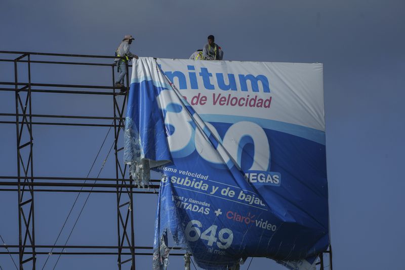 Workers remove an advertisement from a billboard for protection ahead of Hurricane Beryl's expected arrival, in Playa del Carmen, Mexico, Wednesday, July 3, 2024. (AP Photo/Fernando Llano)