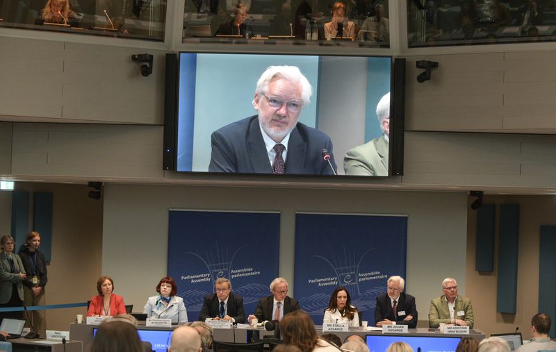 Wikileaks founder Julian Assange is seen an a giant screen as he assesses the Council of Europe while his wife Stella Assange sits next to him, in Strasbourg, eastern France, Tuesday, Oct. 1, 2024. (AP Photo/Pascal Bastien)