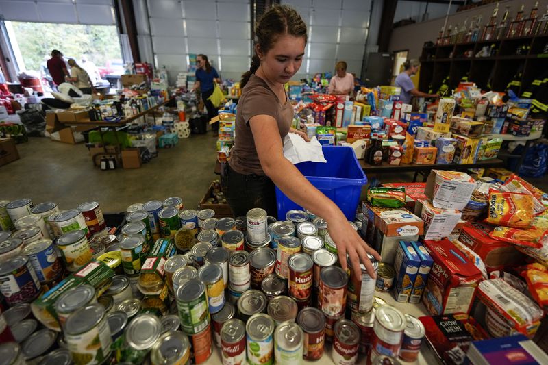 A volunteer gathers food for families at the volunteer fire station in the aftermath of Hurricane Helene, Thursday, Oct. 3, 2024, in Pensacola, N.C. (AP Photo/Mike Stewart)