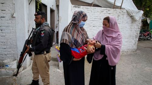 A police officer stands guard as a health worker, right, administers a polio vaccine to a child in a neighbourhood of Peshawar, Pakistan, Monday, Sept. 9, 2024. (AP Photo/Muhammad Sajjad)