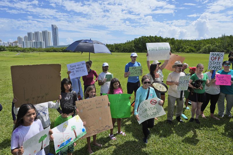 Demonstrators chant during a protest against Gov. Ron DeSantis' plan to develop state parks with business ventures such as golf courses, pickleball courts and large hotels, at Oleta River State Park, Tuesday, Aug. 27, 2024, in North Miami Beach, Fla. (AP Photo/Wilfredo Lee)