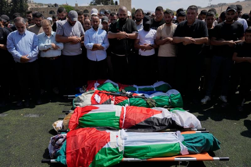 Mourners pray as they attend the funeral of four Palestinians, wrapped in Palestinian flags, who died during an Israeli military operation in the West Bank refugee camp of Al-Faraa, near Tubas, Thursday, Aug. 29, 2024. (AP Photo/Nasser Nasser)