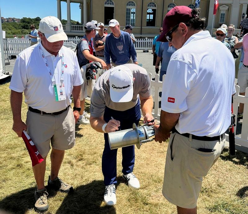 Newport Country Club superintendent Chris Coen, left, and volunteer Joe Oliveria, right, watch as Frank Bensel signs the hole cutter, the blade of which is going to the USGA museum, after Bensel turned up a pair of aces on back-to-back holes during the second round of the U.S. Senior Open golf tournament in Newport, R.I., Friday, June 28, 2024.(AP Photo/Jimmy Golen)