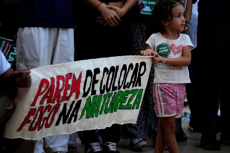 A girl holds a banner with a message that reads in Portuguese: "Stop setting fires in nature", during a global climate protest in Brasilia, Brazil, Friday, Sept. 20, 2024. (AP Photo/Eraldo Peres)