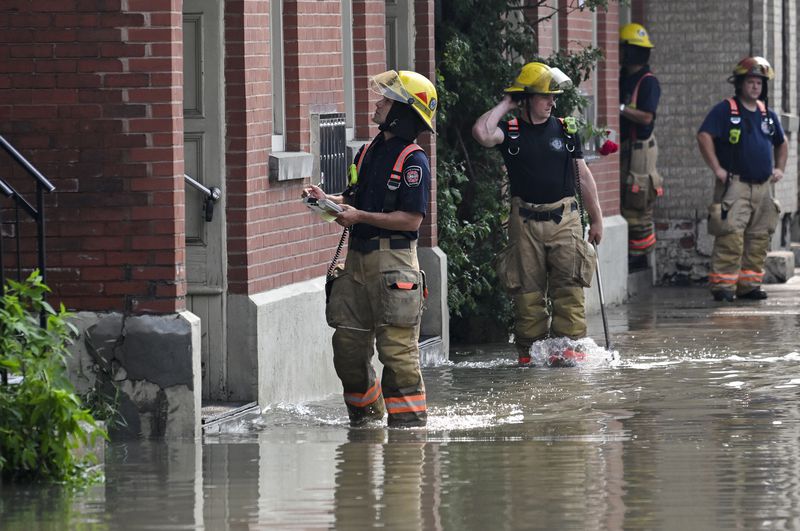 Firefighters check on homes for flooding following a water main break on a street in Montreal, Friday, Aug. 16, 2024, causing flooding in several streets of the area. (Graham Hughes/The Canadian Press via AP)