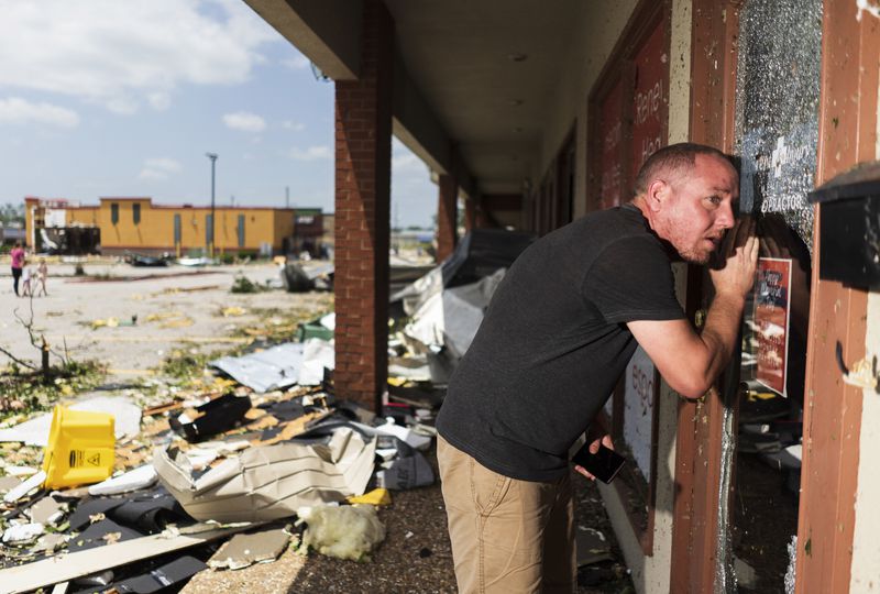 Nathan Whatley of Garfield looks through a store window at a shopping center on West Walnut Ave and North 24th St. Sunday, May 26, 2024, in Rogers, Ark. Powerful storms left a wide trail of destruction across Texas, Oklahoma and Arkansas. (Charlie Kaijo/The Northwest Arkansas Democrat-Gazette via AP)