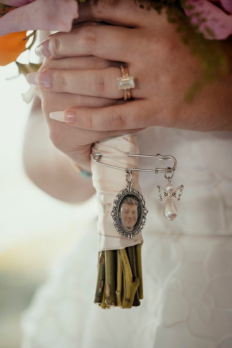 In this image provided by Tell It Well Photography, Gwyneth Collart holds a bouquet with a portrait of her brother the late Marine Corps Cpl. Spencer Collart, during her wedding to Cpl. Jonah Waser, July 6, 2024, in Arlington, Va. Spencer Collart was killed along with two other Marines when the MV-22B Osprey aircraft they were on crashed during drills on a north Australian island on August 27, 2023. (Tell It Well Photography via AP)