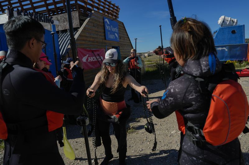 Erin Greene, center, owner of Sup North, hands out equipment before leading a paddleboarding tour, Thursday, Aug. 8, 2024, in Churchill, Manitoba. (AP Photo/Joshua A. Bickel)