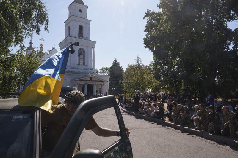 People kneel during the funeral ceremony of six Ukrainian servicemen killed in a Russian rocket attack at a Ukrainian military academy, in Poltava, Ukraine, Saturday Sept. 7, 2024. (AP Photo/Evgeniy Maloletka)