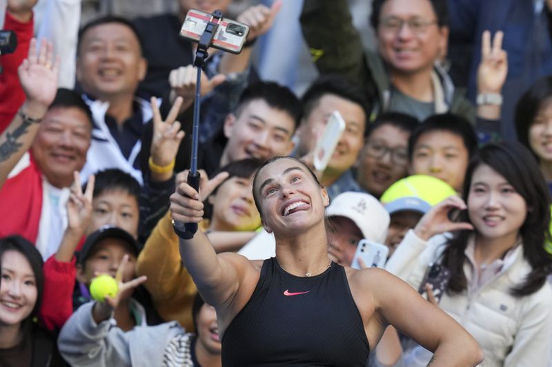 Aryna Sabalenka of Belarus takes a selfie with fans after winning against Madison Keys of the United States during their women's singles match of the China Open tennis tournament, at the National Tennis Center in Beijing, Wednesday, Oct. 2, 2024. (AP Photo/Achmad Ibrahim)