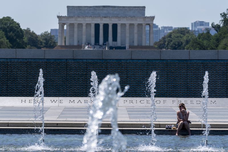 Angie Fagan, from Bassfield, Miss., cools her feet in the Rainbow Pool at the World War II Memorial, with the Lincoln Memorial behind, Friday, June 21, 2024, in Washington. Temperatures are forecast to reach 100 degrees on Saturday. (AP Photo/Alex Brandon)