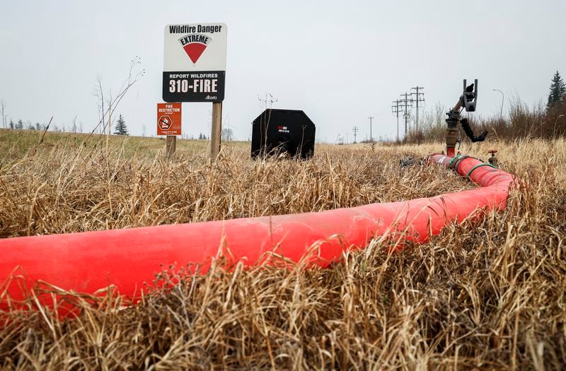 A wildfire danger sign is set to extreme as a hose leads to a wildfire suppression water cannon along highway 881 near Fort McMurray, Alberta, Wednesday, May 15, 2024. (Jeff McIntosh/The Canadian Press via AP)
