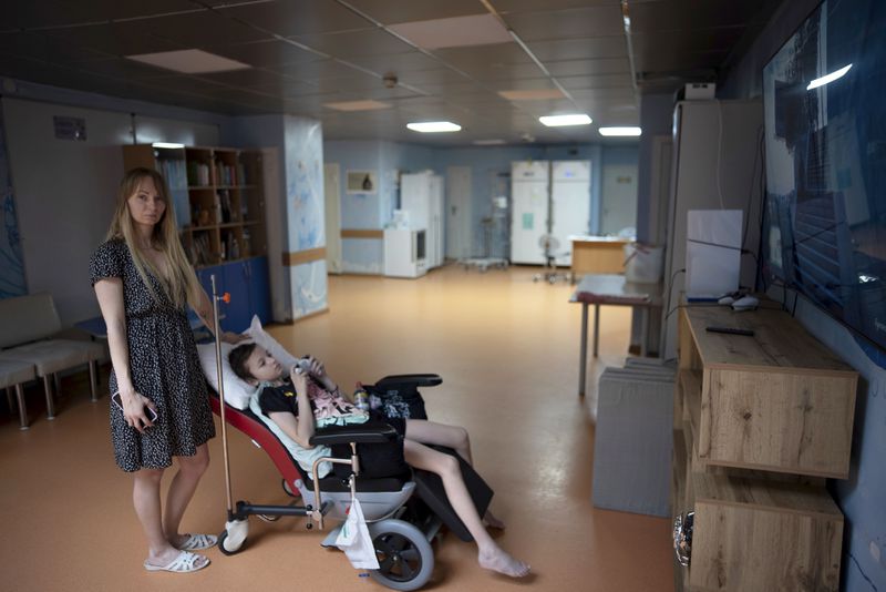 Yuliia Vasylenko poses for a portrait with her son Denys, 11, as he plays on a video game console at the National Cancer Institute in Kyiv, Ukraine, Wednesday, July 10, 2024. Denys is one of 31 young patients battling cancer who were relocated to the hospital from Okhmatdyt Children’s Hospital after it was struck by a Russian missile this week. (AP Photo/Alex Babenko)
