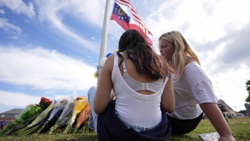 Two students view a memorial as the flags fly half-staff after a shooting Wednesday at Apalachee High School, Thursday, Sept. 5, 2024, in Winder, Ga. (AP Photo/Mike Stewart)