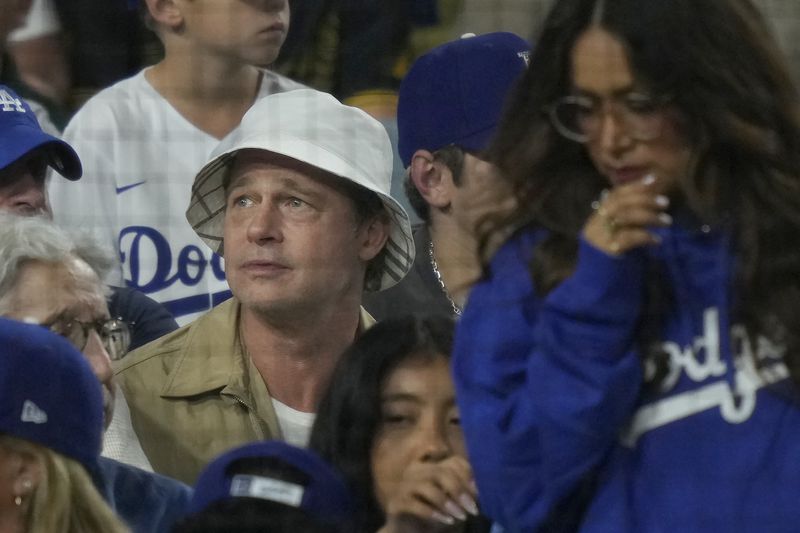 Brad Pitt, in white hat, watches from the stands during Game 1 of baseball's NL Division Series between the Los Angeles Dodgers and the San Diego Padres, Saturday, Oct. 5, 2024, in Los Angeles. (AP Photo/Mark J. Terrill)