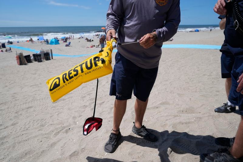An FDNY drone pilot demonstrates an emergency flotation device, carried by some of the drones patrolling the shoreline, at Rockaway Beach in New York, Thursday, July 11, 2024. A fleet of drones patrolling New York City’s beaches for signs of sharks and struggling swimmers is drawing backlash from an aggressive group of seaside residents: local shorebirds. Since the drones began flying in May, flocks of birds have repeatedly swarmed the devices, forcing the police department and other city agencies to adjust their flight plans. (AP Photo/Seth Wenig)