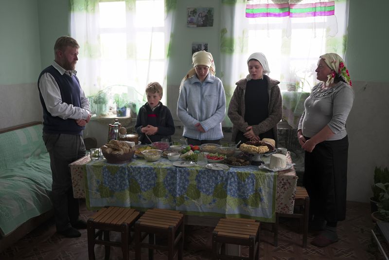 Yuri Strukov, left, his son Ilya, daughters Nina and Daria, and his wife Svetlana Svetlishcheva, right, pray before a meal in their house in the remote mountain village of Orlovka, Georgia, Saturday, May 5, 2024. (AP Photo/Kostya Manenkov)