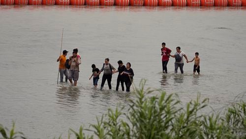 FILE - Migrants who crossed the Rio Grande from Mexico walk past large buoys being deployed as a border barrier on the river in Eagle Pass, Texas, July 12, 2023. The floating barrier is being deployed in an effort to block migrants from entering Texas from Mexico. (AP Photo/Eric Gay, File)