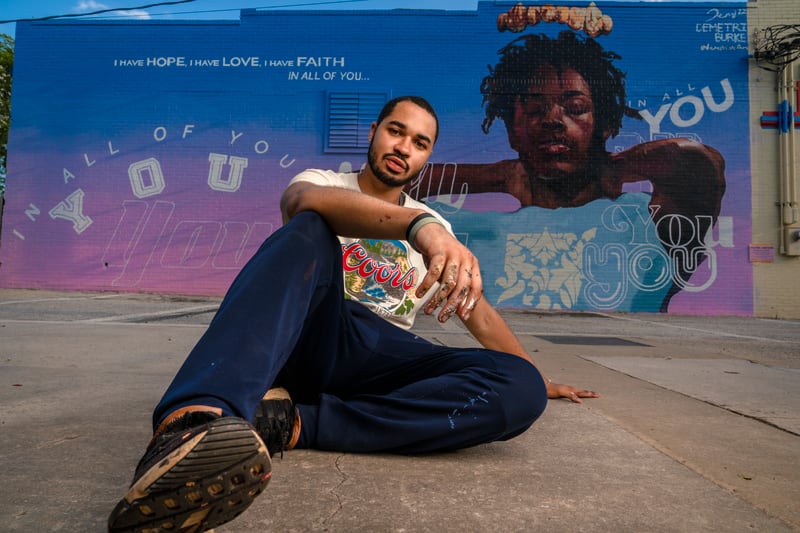 Demetri Burke sits in front of his mural "Come On and Find Me" at Midtown Cleaners. (Brock Scott/On The Grid)