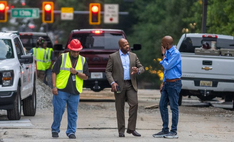 A worker (left) accompanies Watershed Commissioner, Al Wiggins, Jr., (center) and city council member Antonio Lewis (right) confer on West Peachtree Street as workers continued to put the finishing touches on the filled in water main hole Wednesday morning, June 5, 2024 following the city’s announcement that water had been restored following the break on West Peachtree Street and 11th Street. The city said the system was being brought back online slowly to “allow system pressures to build.” (John Spink/AJC)